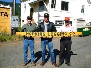 In 2003, I traveled to Greeville. Here, my high school friends, Mike
Knadler on left, and John Hunter on right, pose with the Hopkins Logging
Company logo crosscut saw that once hung on the Hopkins Logging Company
office building in Greenville. John secured it from a garage sale, saved
it, and gave it to me years later. I was astonished when I met up with
the old saw
again.